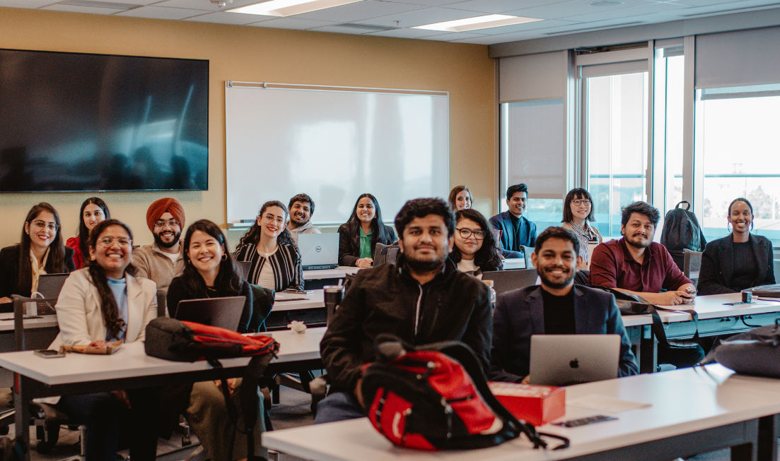 A large group of students at desks all smiling at the camera.