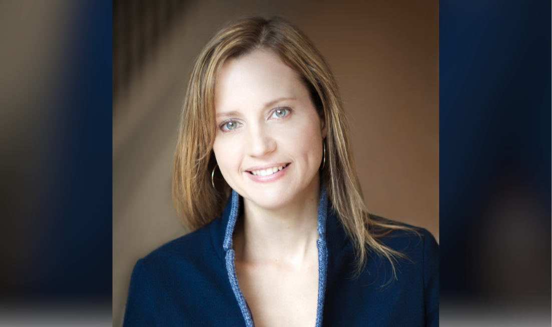 Head and shoulders of Samantha Nutt, a smiling woman with brown hair wearing a blue blazer over a white top, against a dark background.