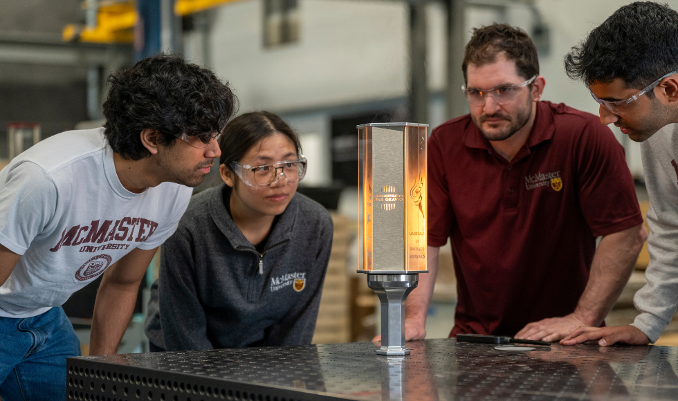 Four people wearing protective eye glasses looking intently at a commemorative torch.