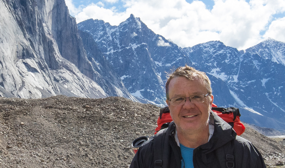 Doug Welch head and shoulders in the foreground, against a backdrop of towering snow-capped mountains.