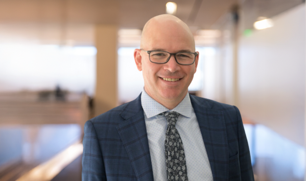 Waist-up shot of Mike Heenan, smiling at the camera in a hallway of the DeGroote School of Business.