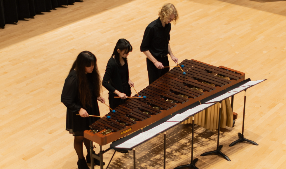 Seen from above, three students standing side by side play the marimba.