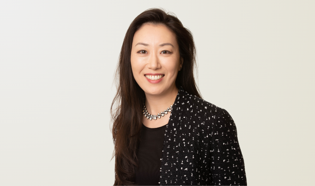 Headshot of Ruth Chen, smiling, wearing a necklace, dark top with a dark jacket over it.