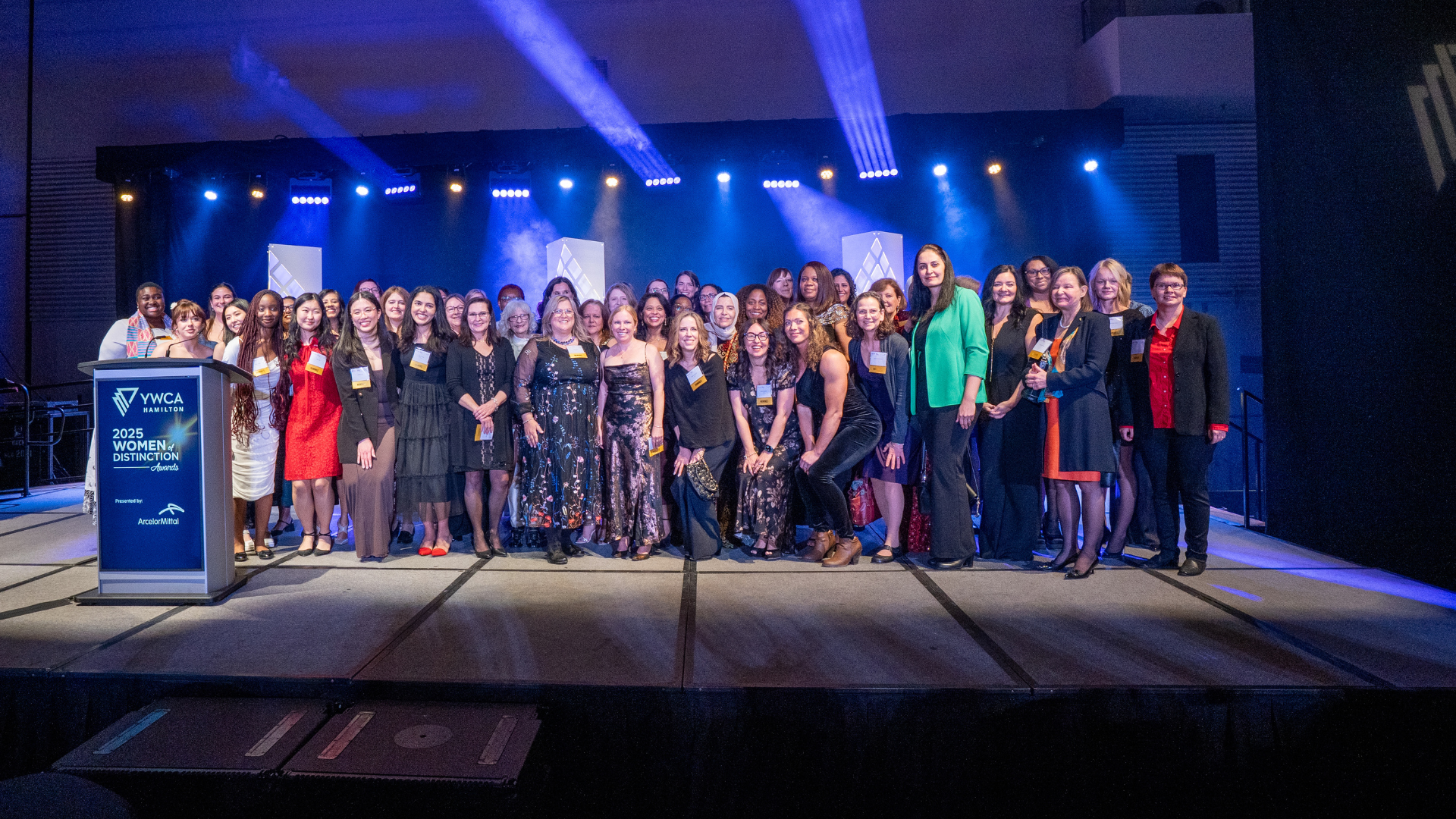 A group of approximately fifty women stand on a stage at a gala.