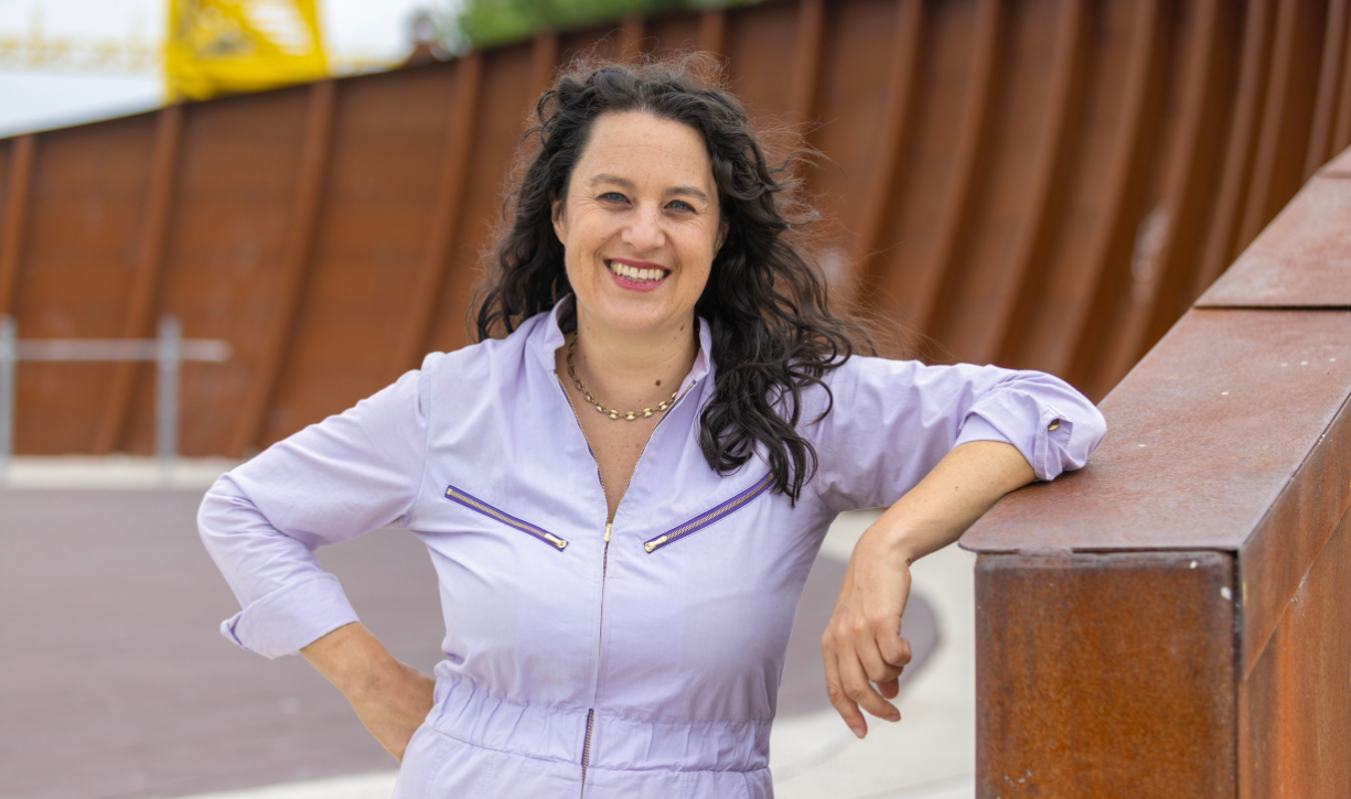 A woman in a lilac shirt smiles and leans against a wooden railing.