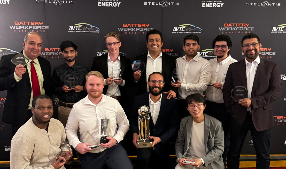 Eleven people stand in front of a backdrop that reads 'Battery Workforce Challenge.' They are all holding trophies.