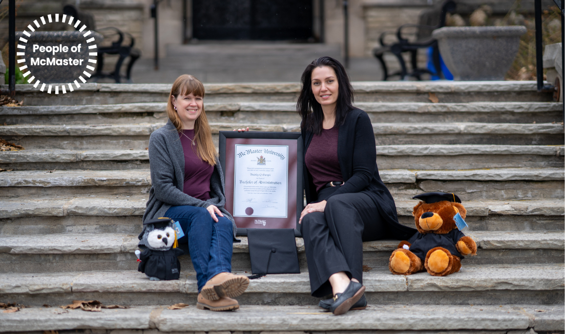 Diane Warwick and Kimberly Foottit sitting on the stone steps of a university building, holding up an example of a framed McMaster degree and flanked by commemorative graduation stuffed toys.