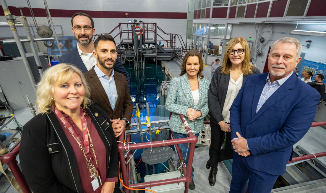 Six smiling people standing inside McMaster's nuclear reactor