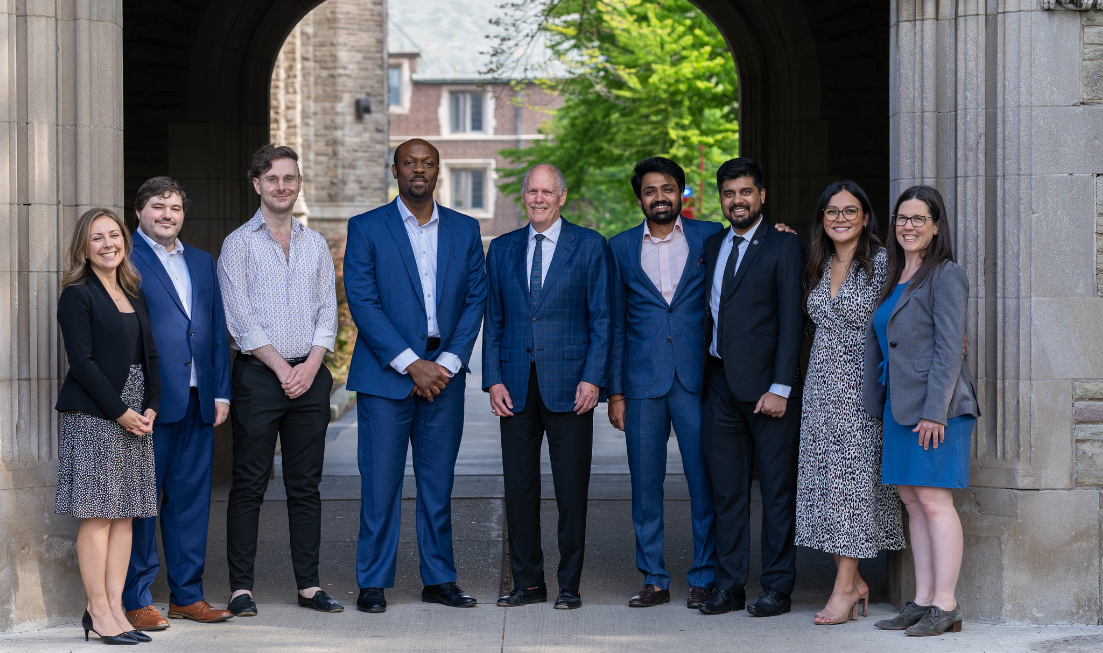 Smiling university president David Farrar in the middle of a group of eight others, under the University Hall arch at McMaster.