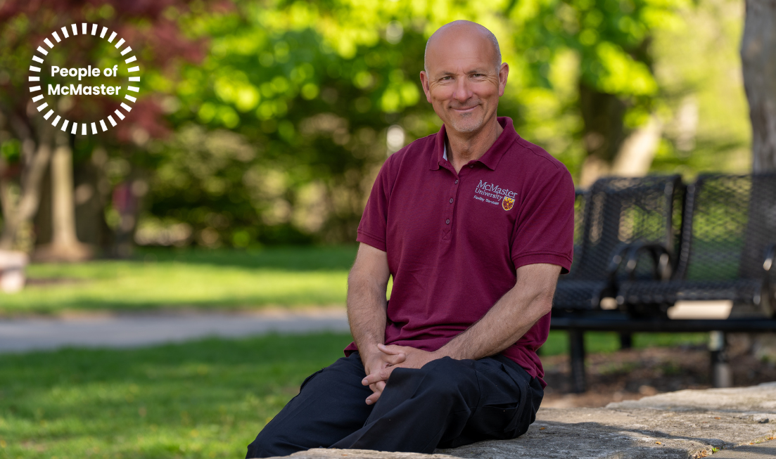 Gary Moscardini, wearing a maroon McMaster shirt, sitting outdoors on campus on a sunny spring day.