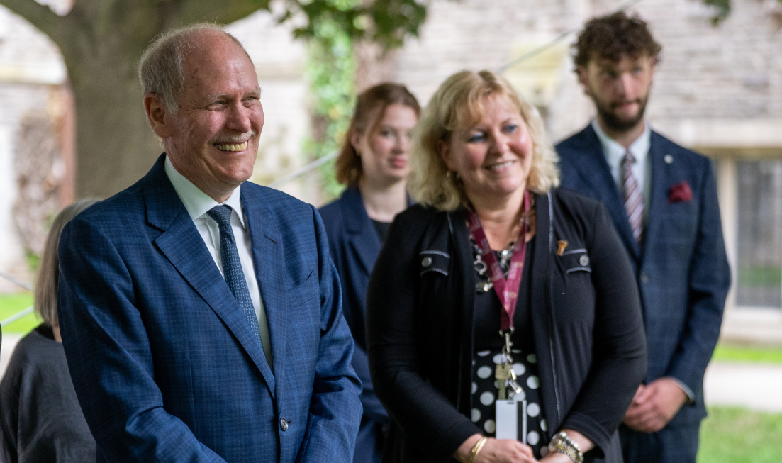A smiling David Farrar and Susan Tighe in the foreground, standing outdoors. In the background are two students.