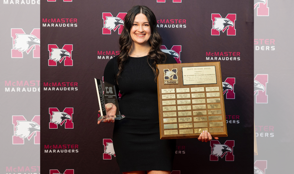 A woman holds a trophy and a large award plaque.