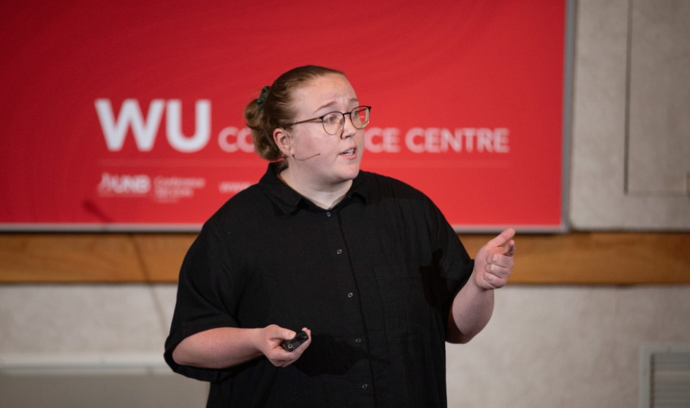 A woman speaks in front of a red poster.