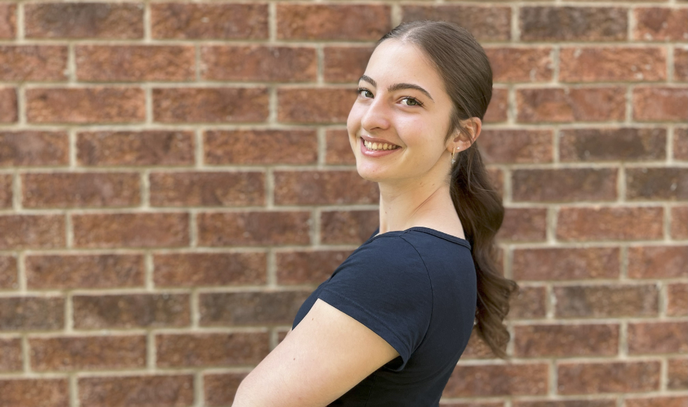 A young woman smiles at in front of a brick wall.