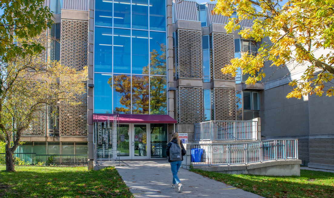 Seen from behind, a student walks toward the doors to Mills Memorial Library on a fall day.