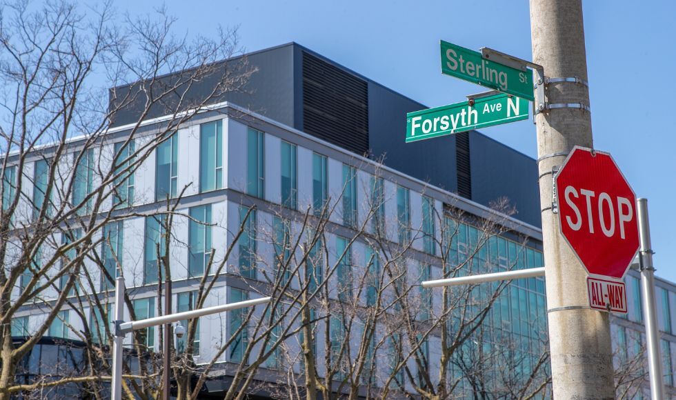 A grey pole holds a stop sign, and two street signs that read 'Sterling St' and 'Forsyth St N'. A large building is visible in the background.