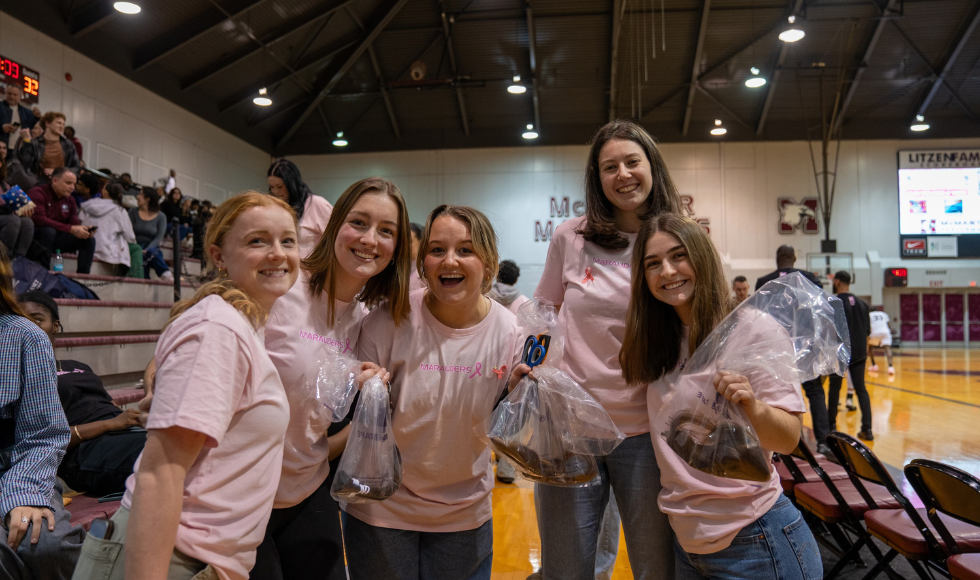 Five women in pink t-shirts stand at the edge of a basketball court.