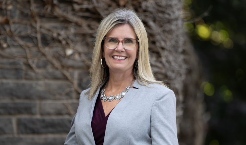 A woman wearing a grey blazer smiles to camera.