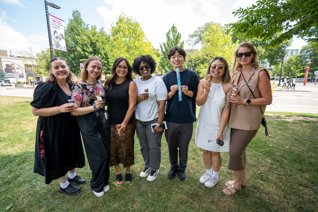 A group of people stand outside on a summer's day, holding up ice cream and freezies.