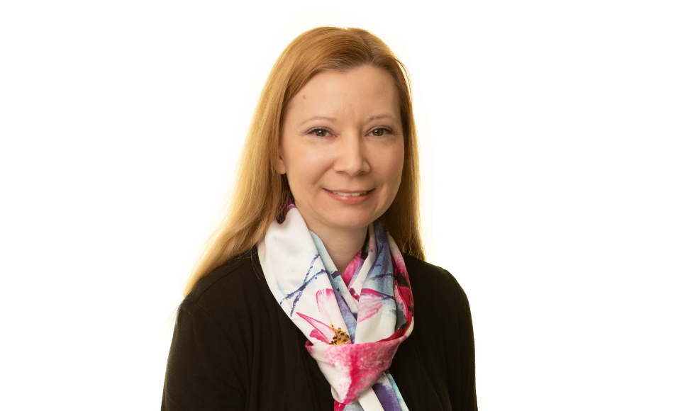 A woman facing camera smiles, wearing a scarf and black sweater.