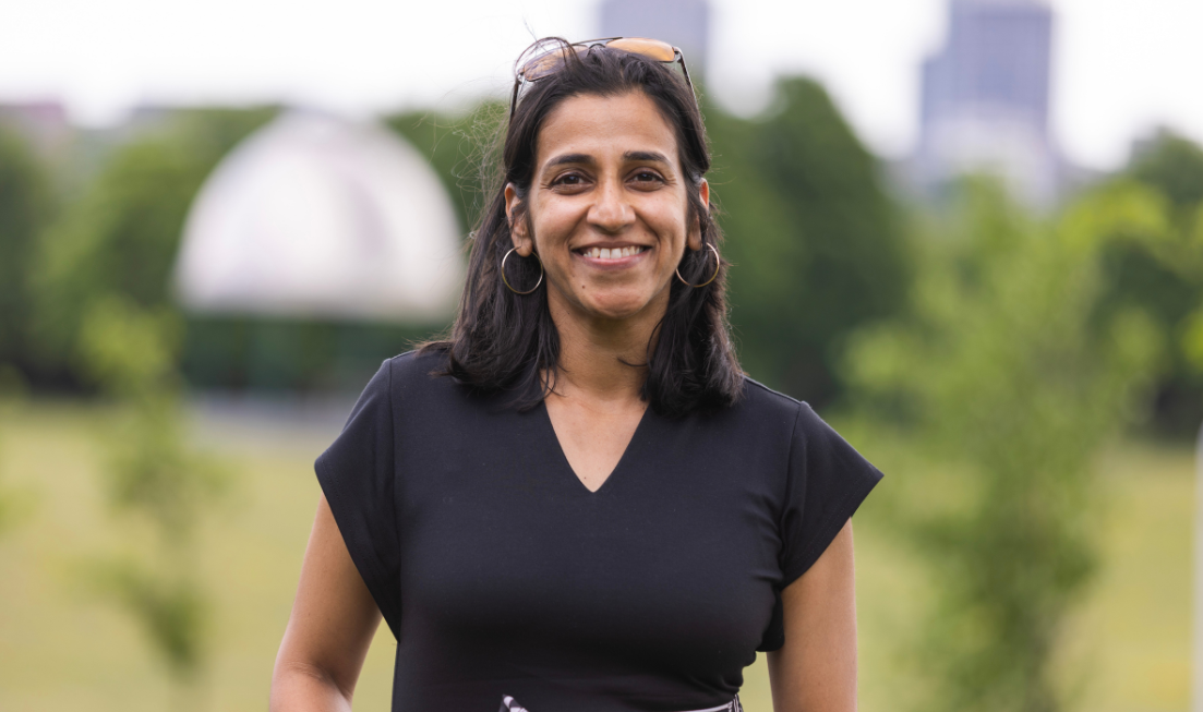 A smiling woman in a dark top with her sunglasses on the top of her head.