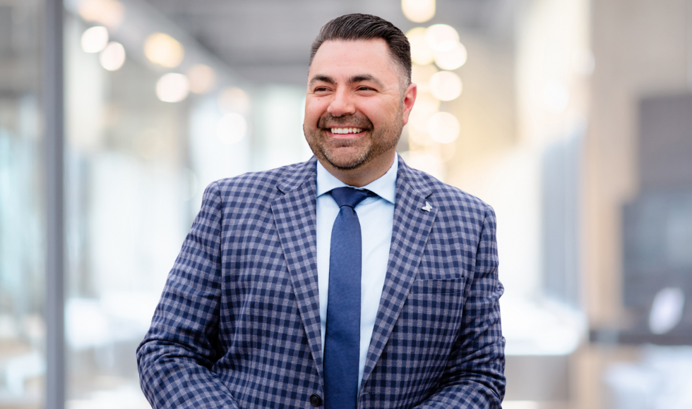 Tej Sandhu, wearing a suit and tie, smiling as he looks to the side of the camera.
