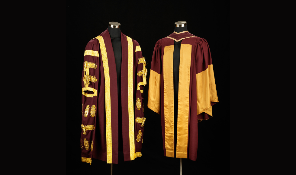Two ceremonial robes hang on stands against a black background.