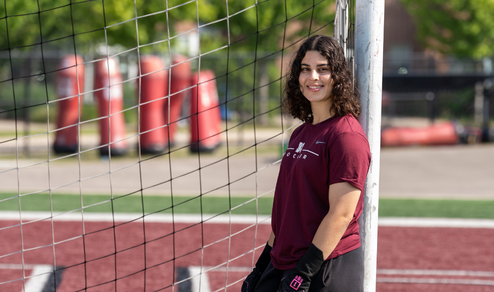 A woman leans against a soccer net.
