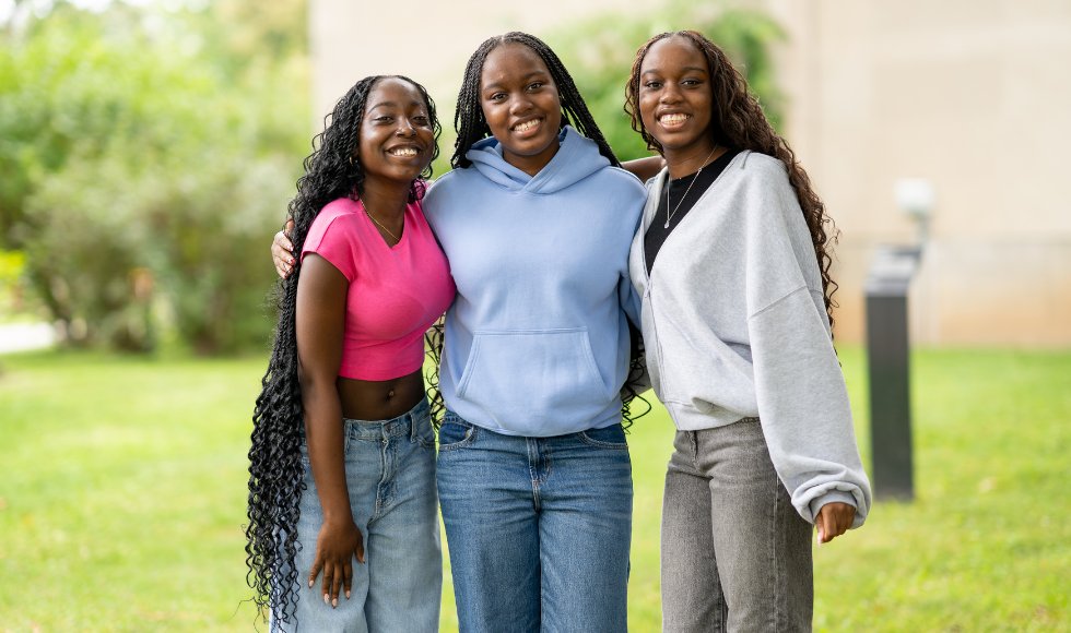 Three women stand with their arms around each other, posing for the camera.